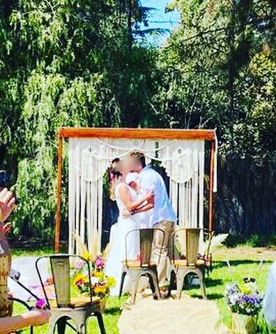 Novios besándose bajo arco de macramé